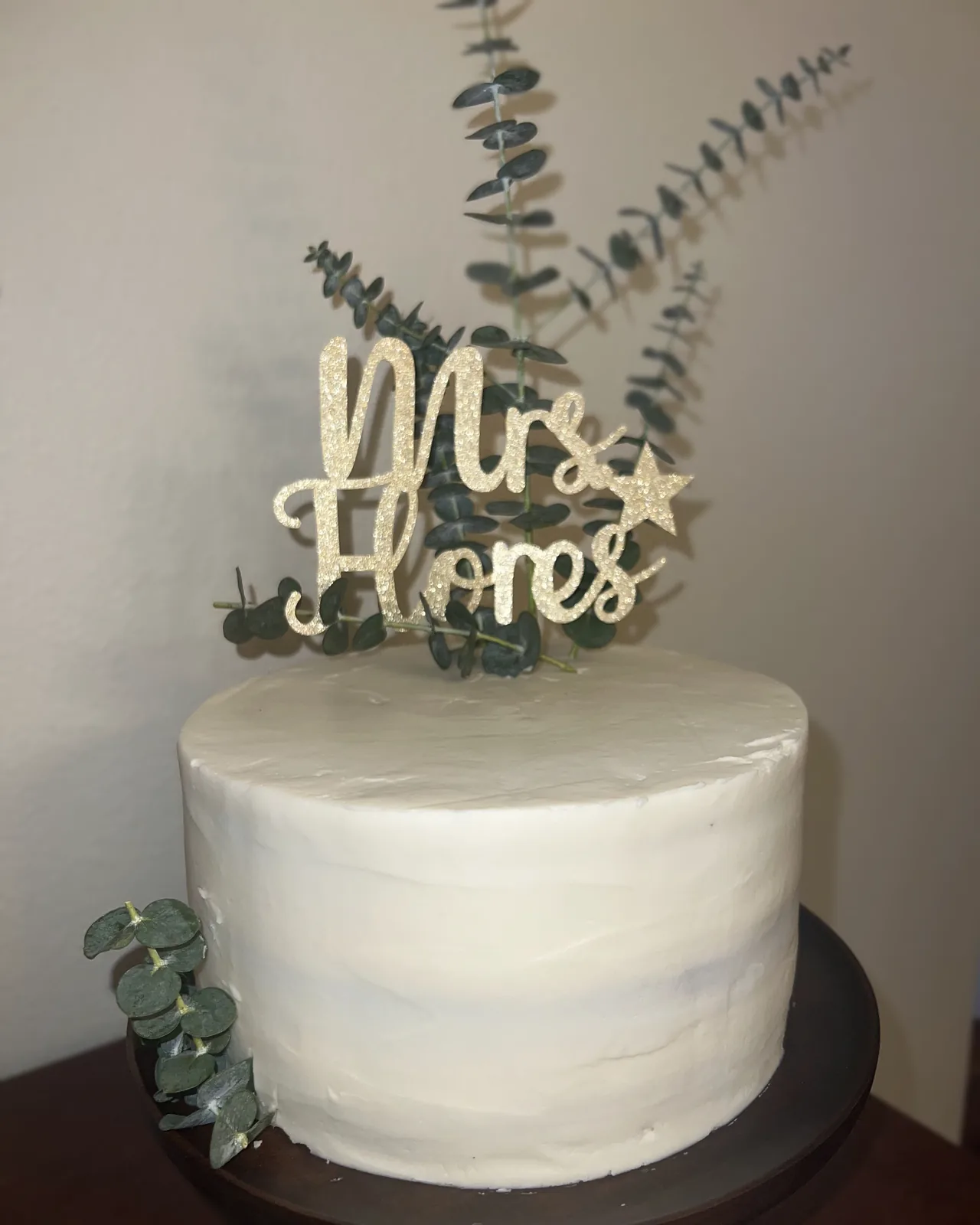 White cake with greenery and glitter topper